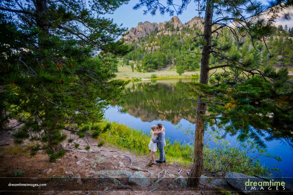 A bride and groom embrace on the shore of Lily Lake, Colorado